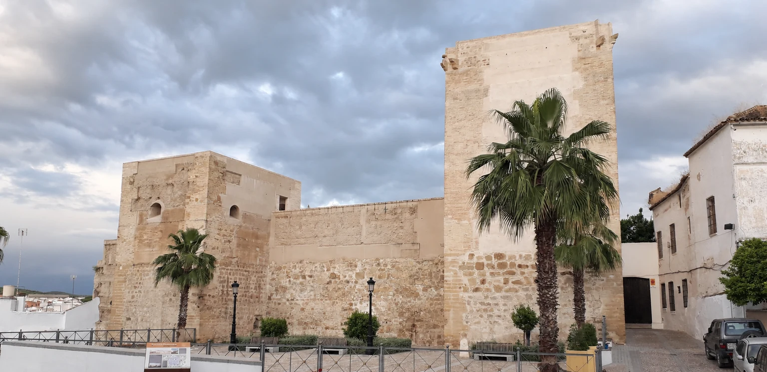 Torres y muralla del castillo de Castro del Río, con palmeras y las casas del entorno.