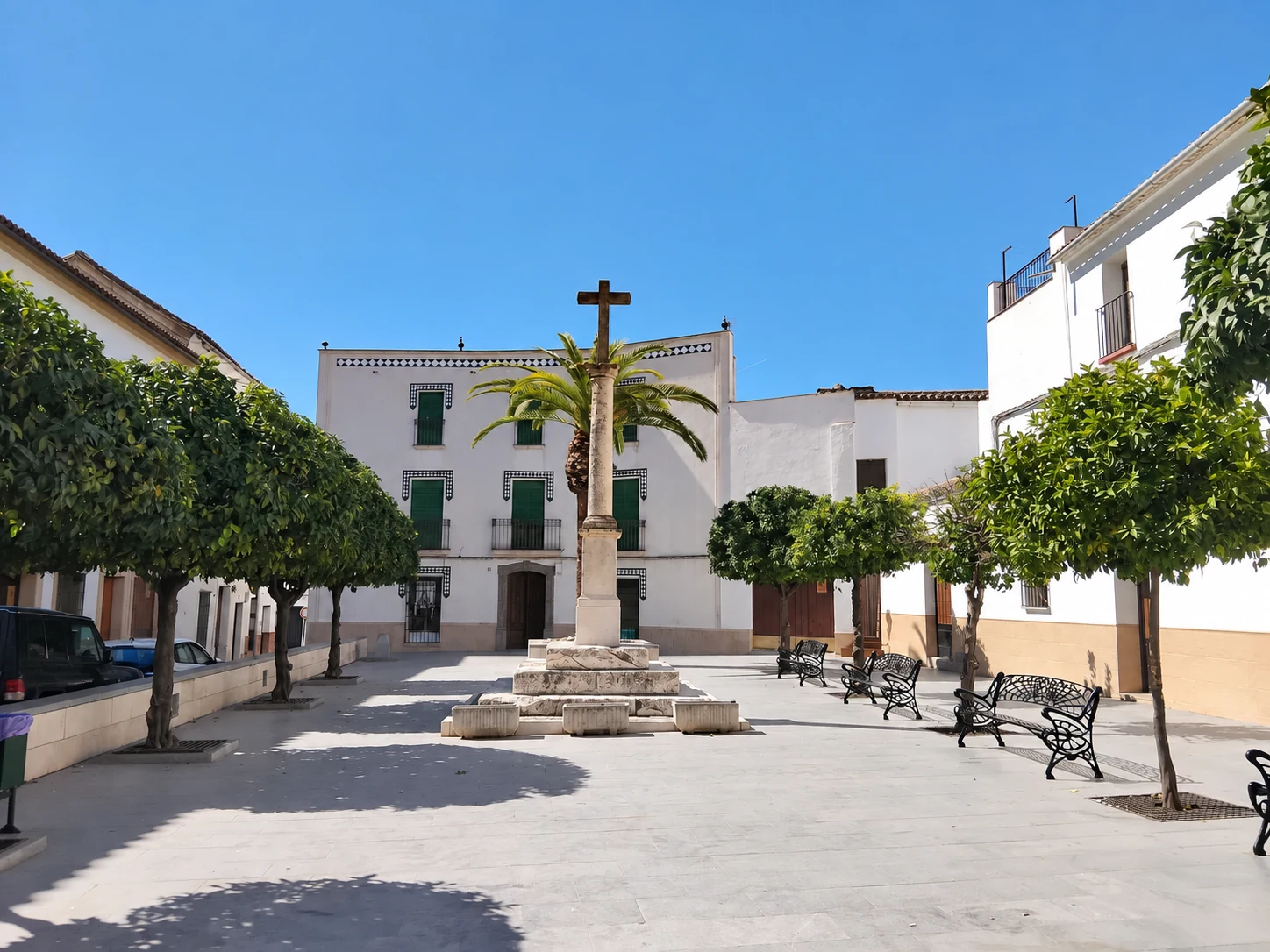 Plaza de la Iglesia de Castro del Río, con su cruz de piedra, naranjos, bancos y fachadas blancas.