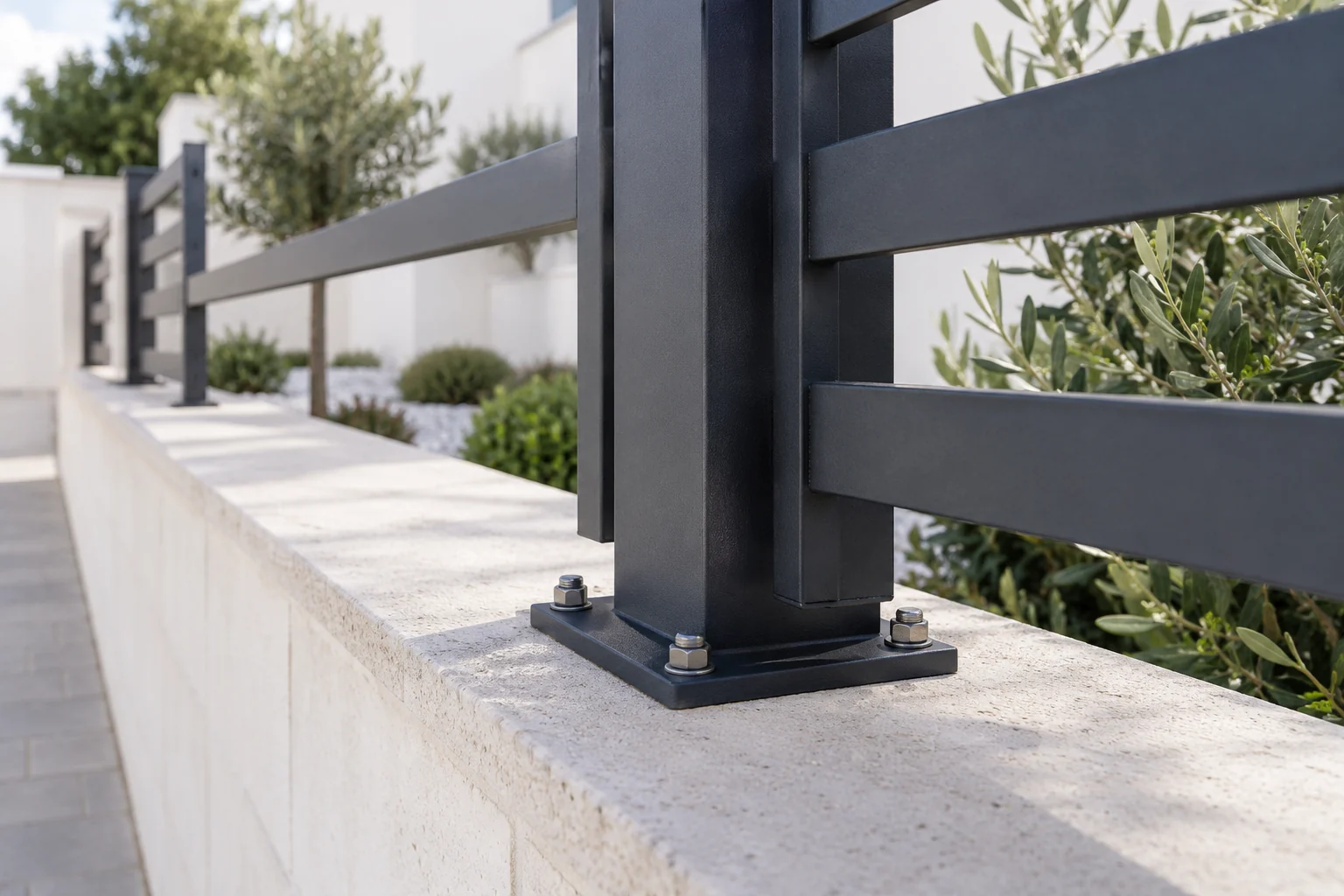 Poste y base de una valla metálica instalados sobre un murete claro.